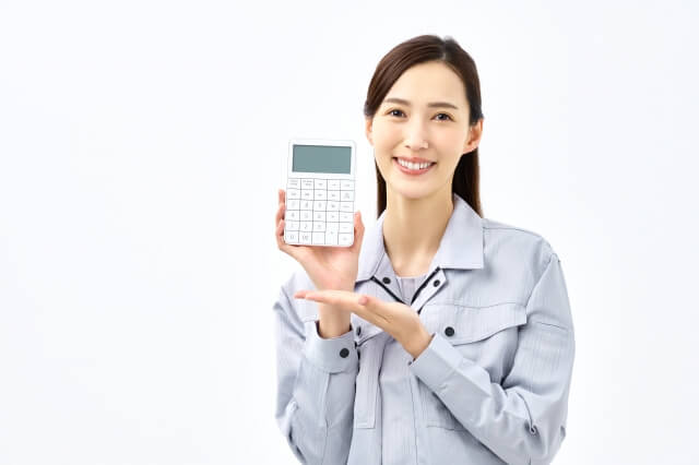 電卓を持って笑顔でこちらに見せる作業着の女性