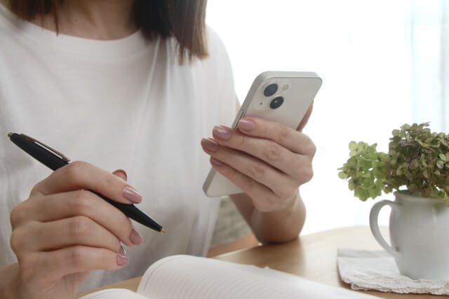 メモを取りながらスマホをスマホを見る女性
