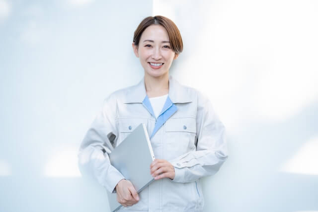 パソコンを小脇に抱えて微笑む作業着の女性