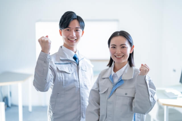 ガッツポーズをする作業着を着た男女