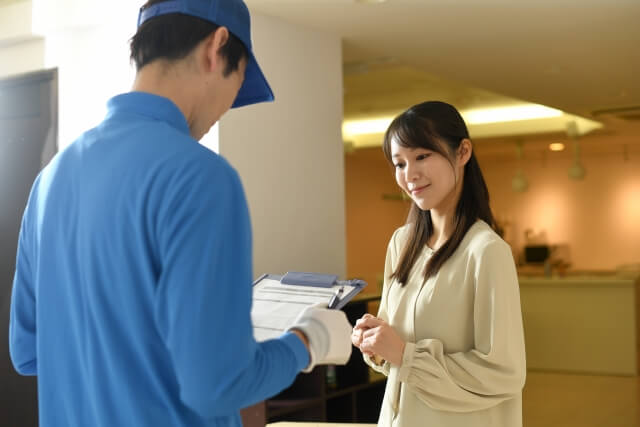 帽子を被ったバインダーを持った作業着の男性が女性に説明している